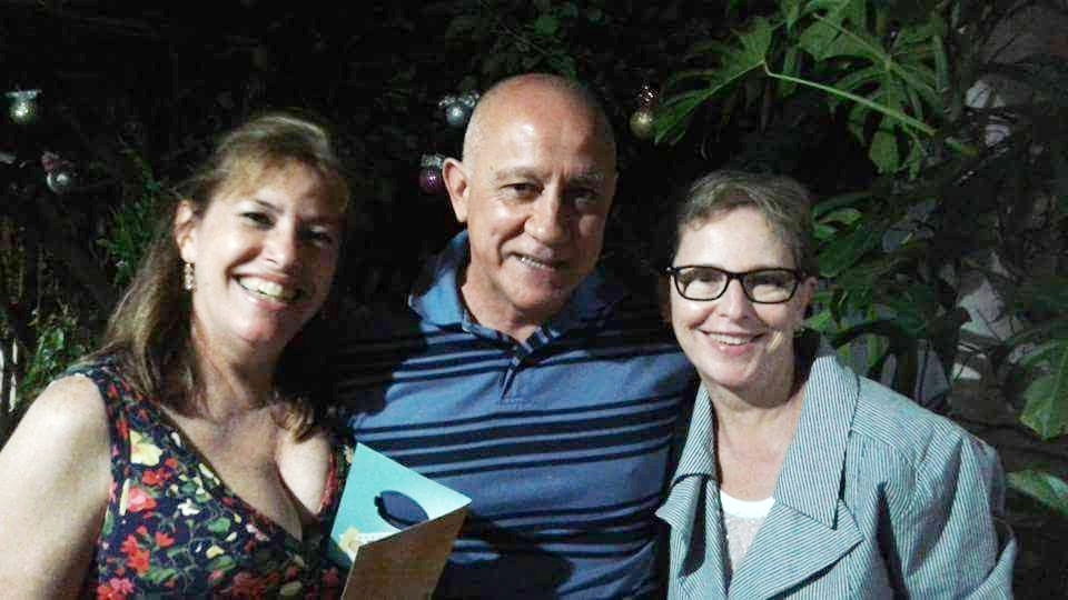 Foto horizontal, duas mulhere e um homem entre elas, os três sorrindo
