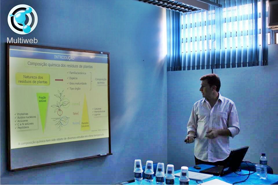 Foto quadrada de pessoa apresentando trabalho em frente à tela de projeção
