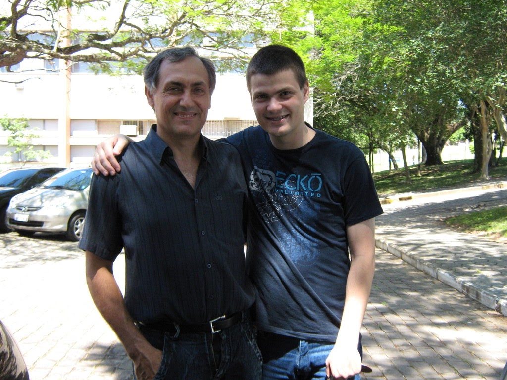 Foto horizontal, um senhor e um rapaz novo abraçados em frente a um dos prédios da UFSM
