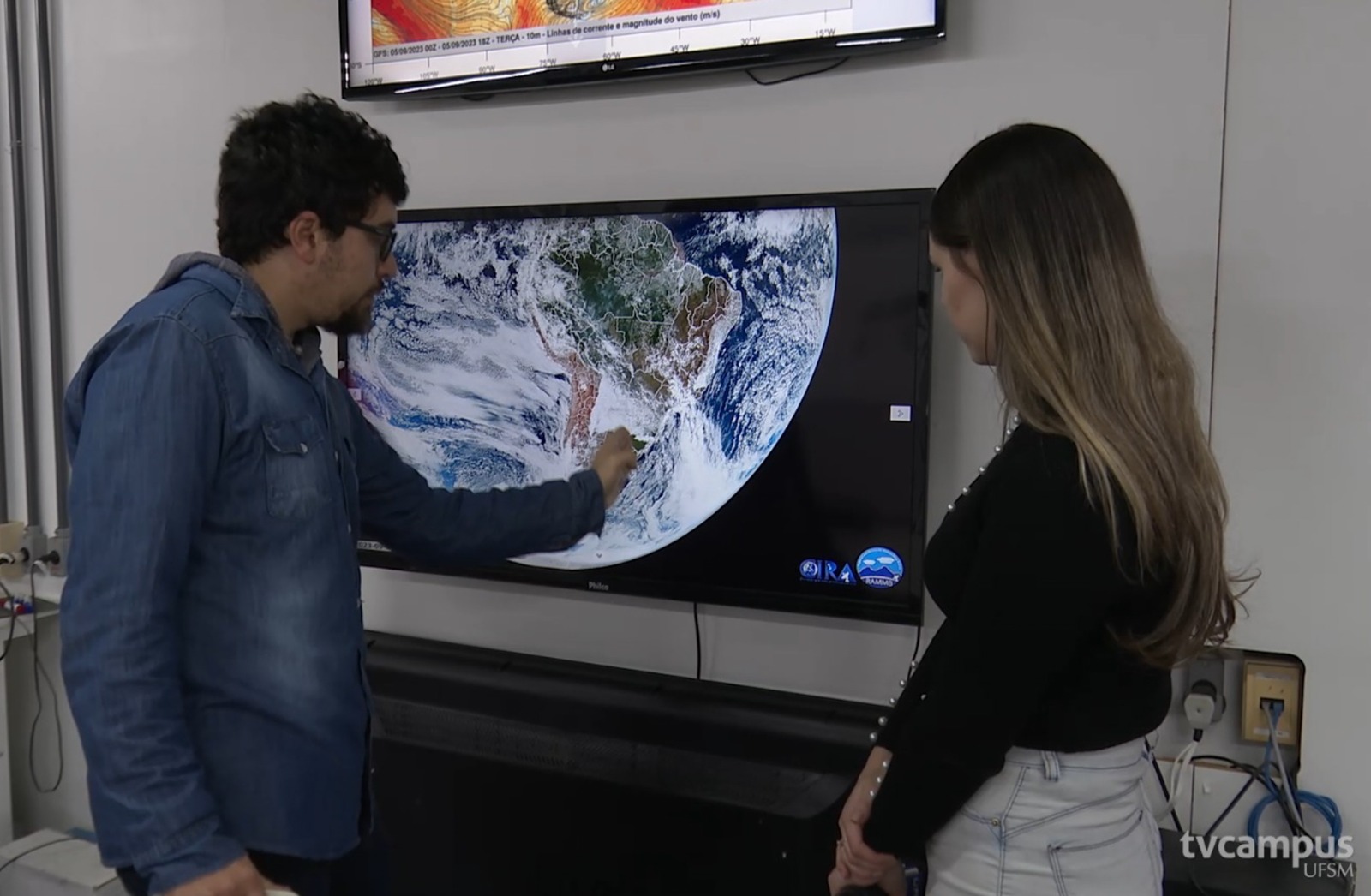 foto colorida com um homem e uma mulher analisando um globo terrestre em uma tela de TV