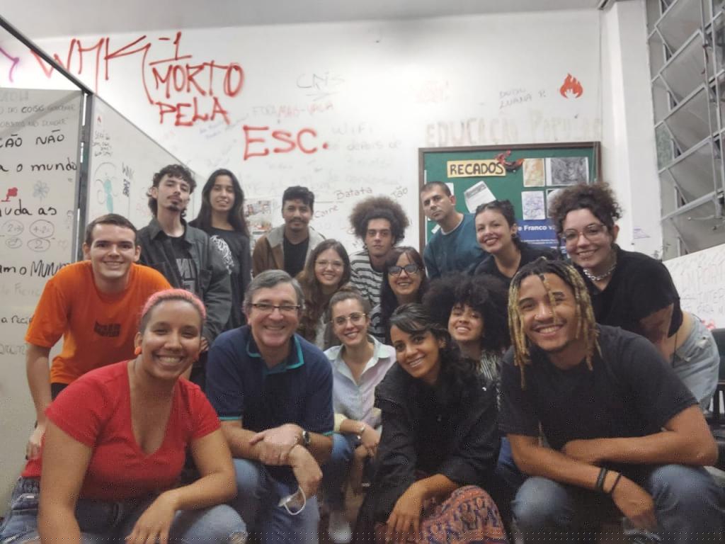 Foto colorida horizontal de várias pessoas agachadas e posando para a câmera. O grupo é composto de mulheres e homens