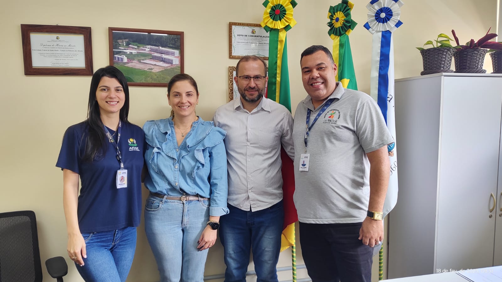 Foto coloridade horizontal de quatros pessoas em pé posicionadas uma ao lado da outra. Na imagem, duas mulheres, uma de cabelo solto e a outra de cabelo preso, e dois homens. 