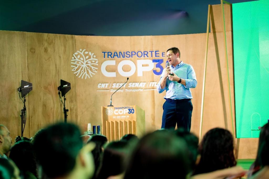 Foto colorida horizontal do professor Deivid em pé, com roupa social, com microfone em punho no palco do evento. Atrás dele, um painel escrito COP30. Do lado esquerdo, um púlpito de madeira. À frente, a plateia.