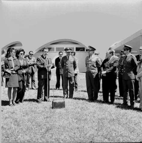 Descrição da imagem: Fotografia quadrada e em preto e branco de 12 homens e duas mulheres, em pé, em formato de meia lua, estão em torno de um bloco pequeno de concreto, que está sobre o gramado. No fundo, detalhe da cúpula do Planetário da UFSM.