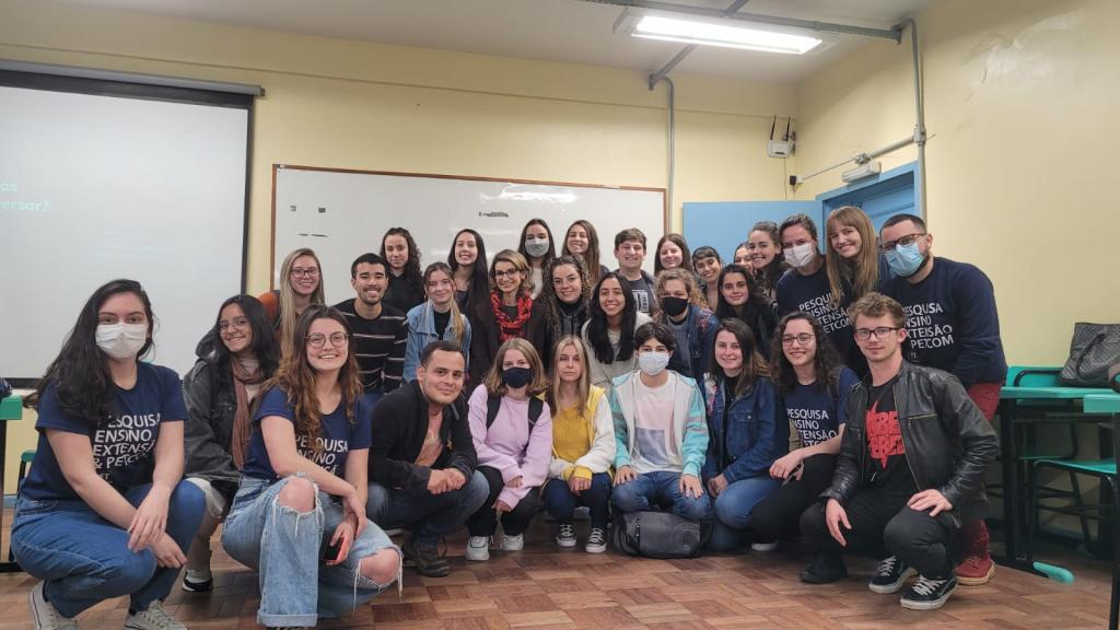 30 pessoas agrupadas na fotografia. Petianos e petianas estão identificados com a camiseta e moletom azul do PETCom, ao centro está nossa ministrante Juliana Motta.