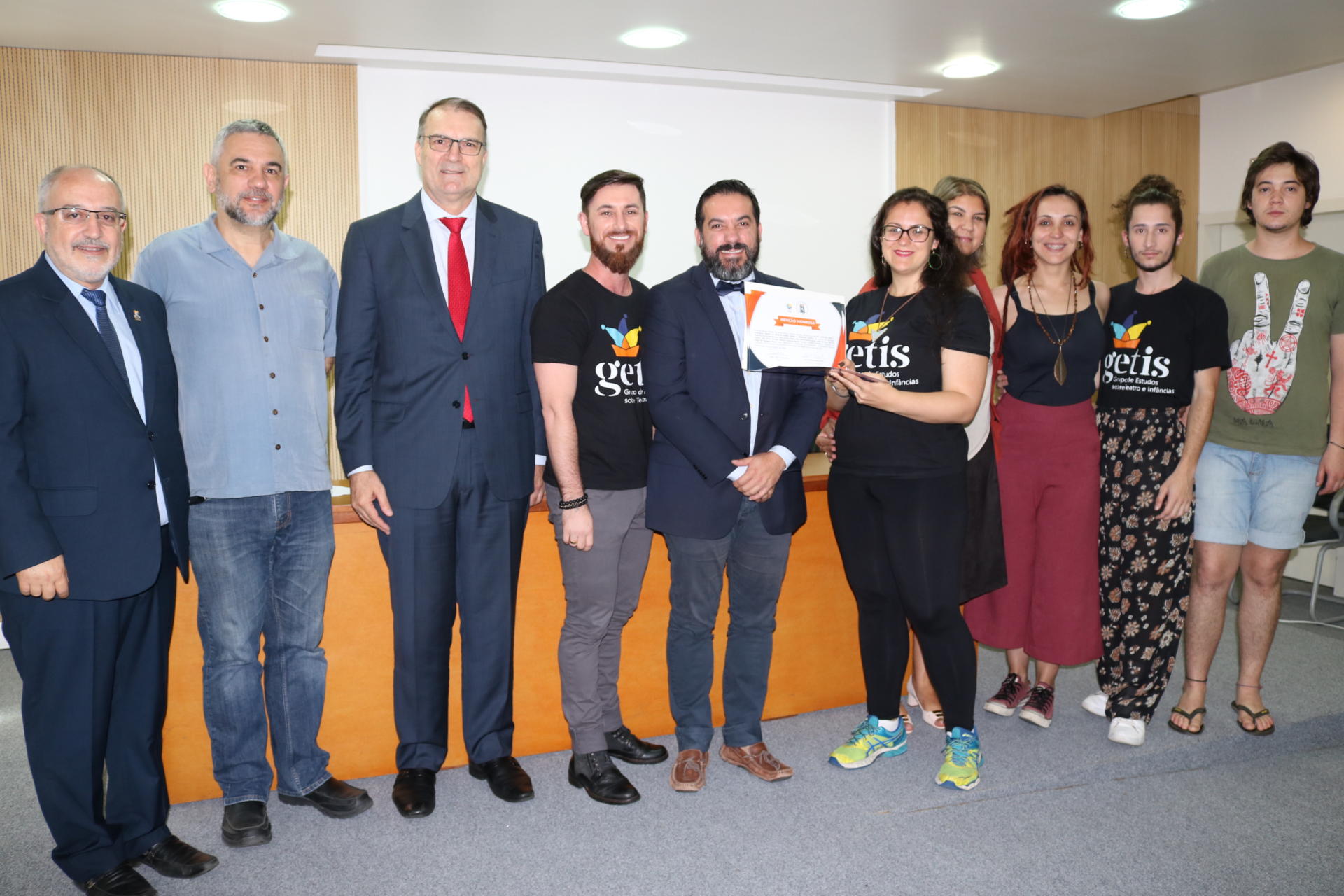 Dez pessoas à frente do palco, incluindo o reitor e o pró-reitor de Extensão. Uma das alunas segura o certificado