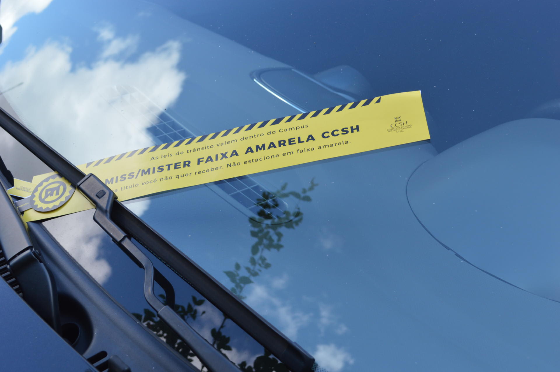 Foto de uma faixa da campanha, em amarelo, colocada sobre o parabrisa de um carro