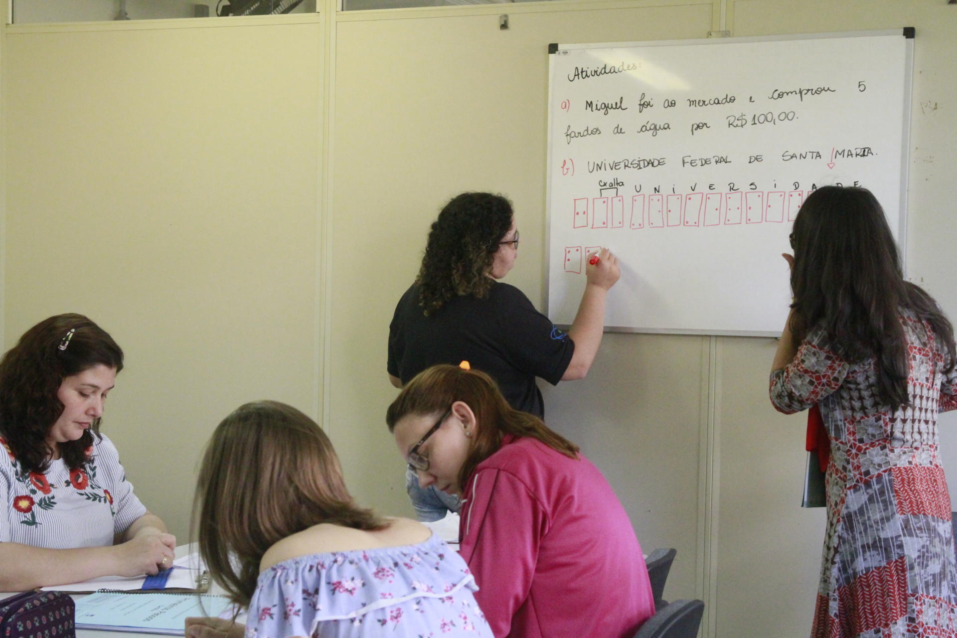 Foto colorida horizontal em que participantes do curso desenham símbolos de Braille em um quadro