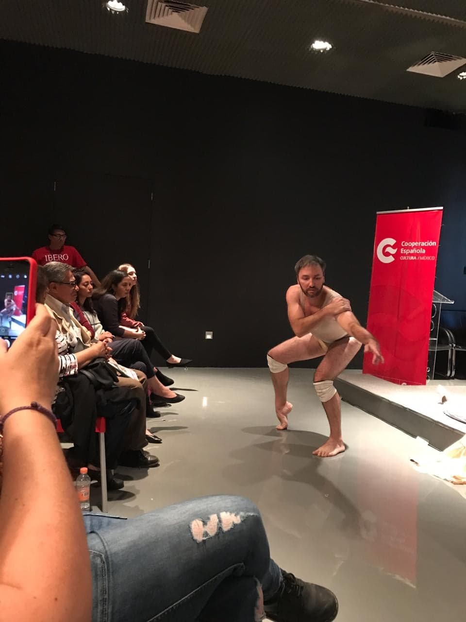 Foto vertical colorida mostrando o professor Berté durante sua performance em um espaço interno, próximo ao público que o assiste