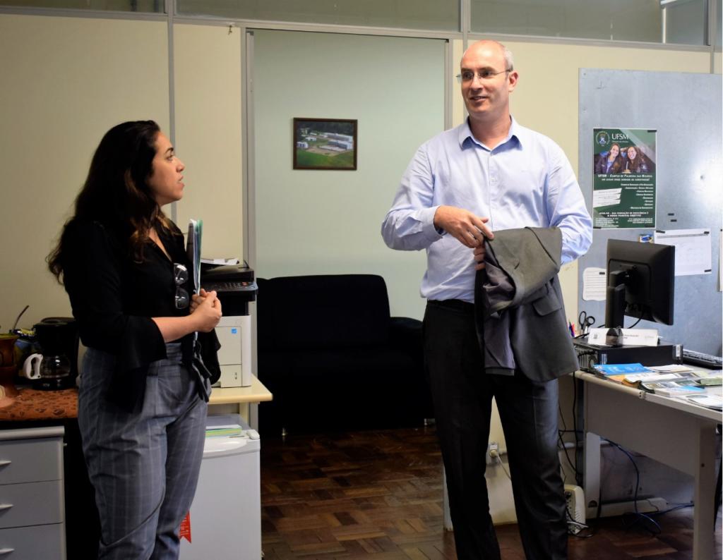 Foto horizontal, em cores, da pró-reitora e do vice-reitor. Os dois estão em pé. A pró-reitora olha para o vice-reitor, que está falando sobre algo