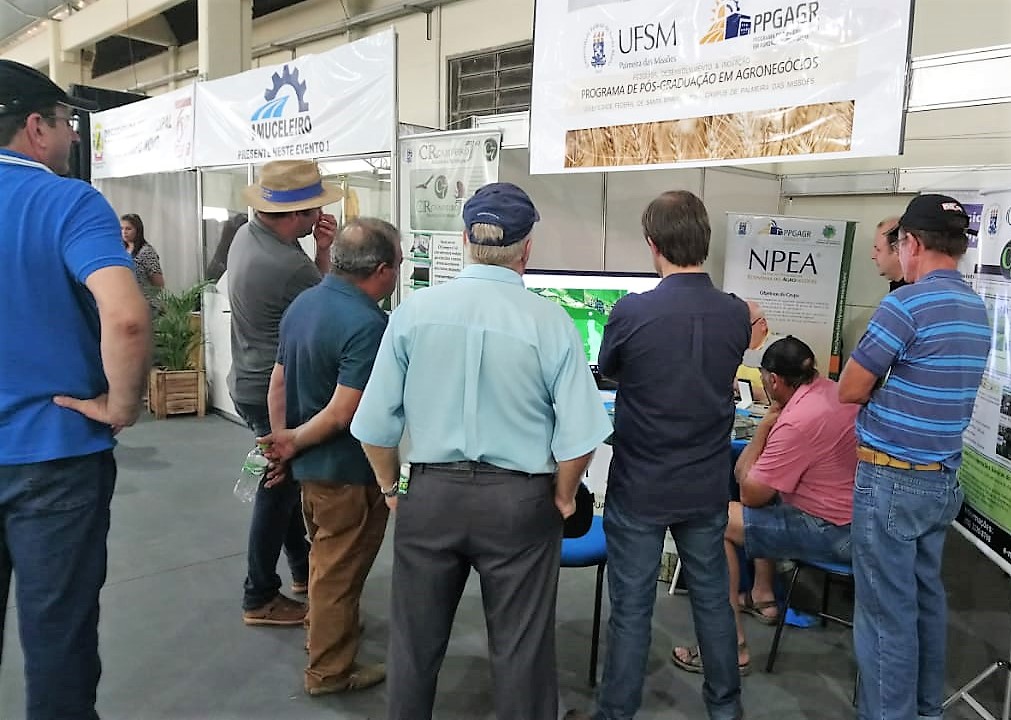 Foto colorida horizontal mostra visitantes ao redor de um estande da UFSM no evento