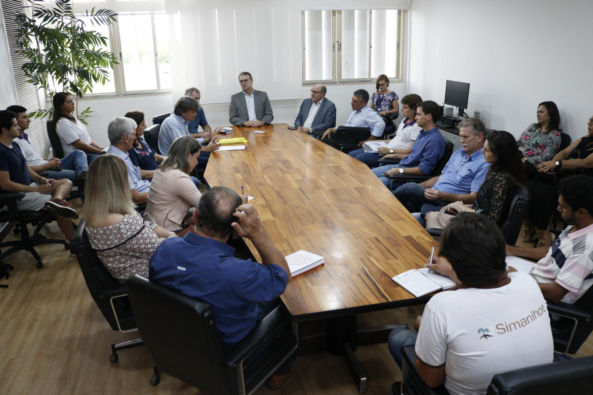 Foto colorida horizontal mostra o reitor sentado na cabeceira da mesa, e outras pessoas ao redor